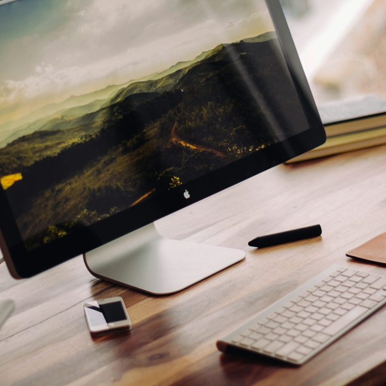 A modern desktop setup featuring a large monitor, keyboard, mouse, and notebook.