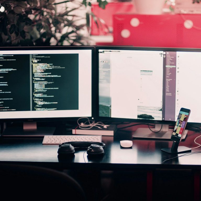 A workspace with dual monitors displaying code and a smartphone on a desk.