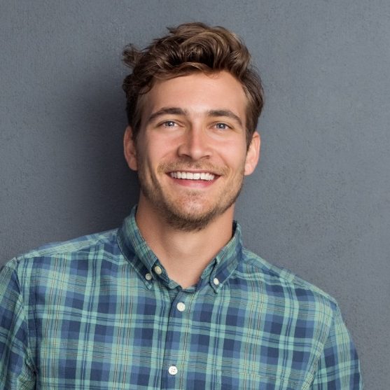 Smiling man with curly hair in a checkered shirt against a grey background.